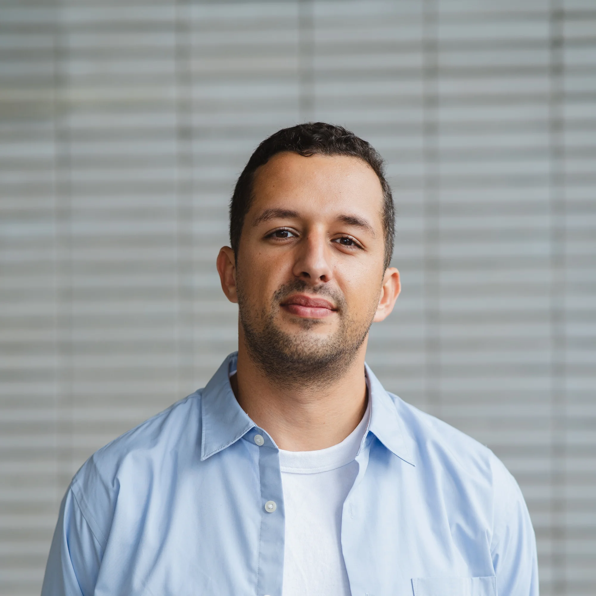 Ilias Azdoufali, manager bij Studio Renders, poseert in lichtblauw hemd voor een grijze achtergrond